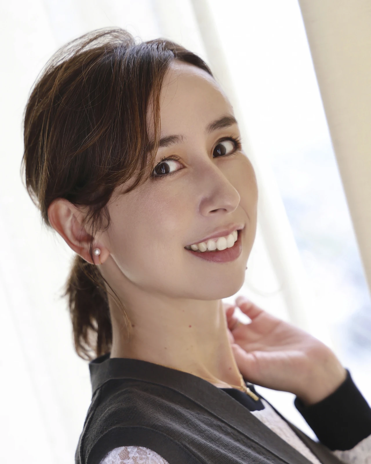 窓辺で首元に手を添え、こちらに微笑む岡田マリア